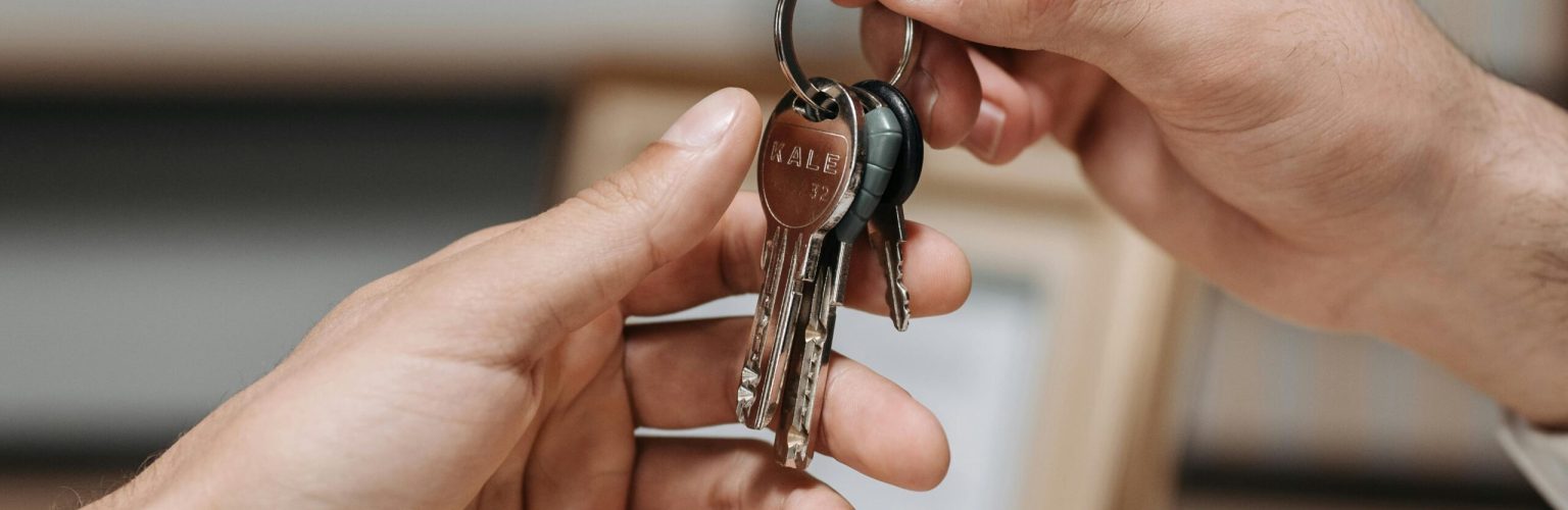 A close-up image of two hands exchanging a set of keys indoors.